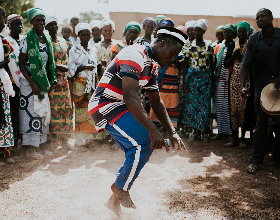Kenyan man dances outside while other stand in a circle watching