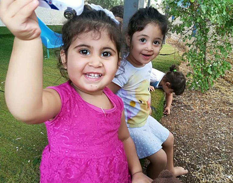 Two little Palestinian girls sitting on the ground one holding up a toy car