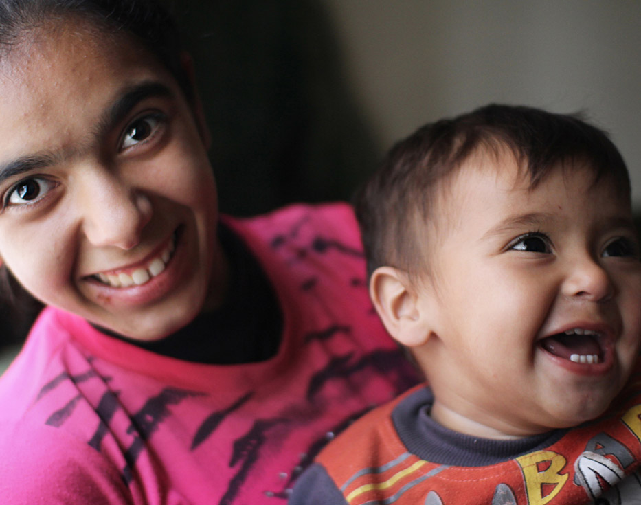 Lebanese girl sits smiling with her little brother sitting on her lap
