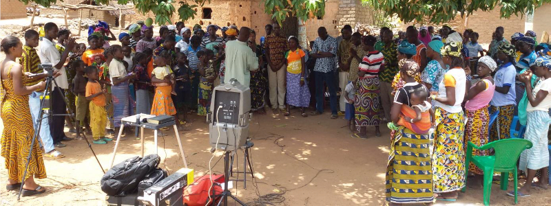 Burkinabé pastor preaches outside in a dusty climate to a group of Christians