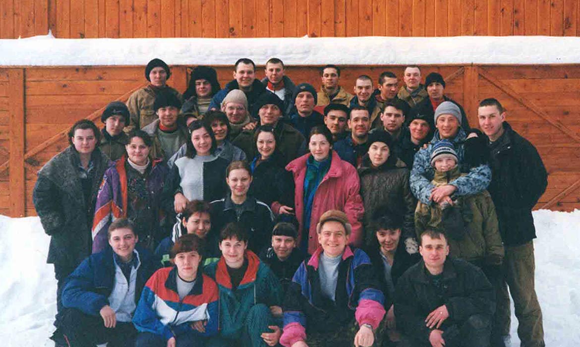 Russian Christians in winter clothes standing in front of a wooden fence with snow on the ground