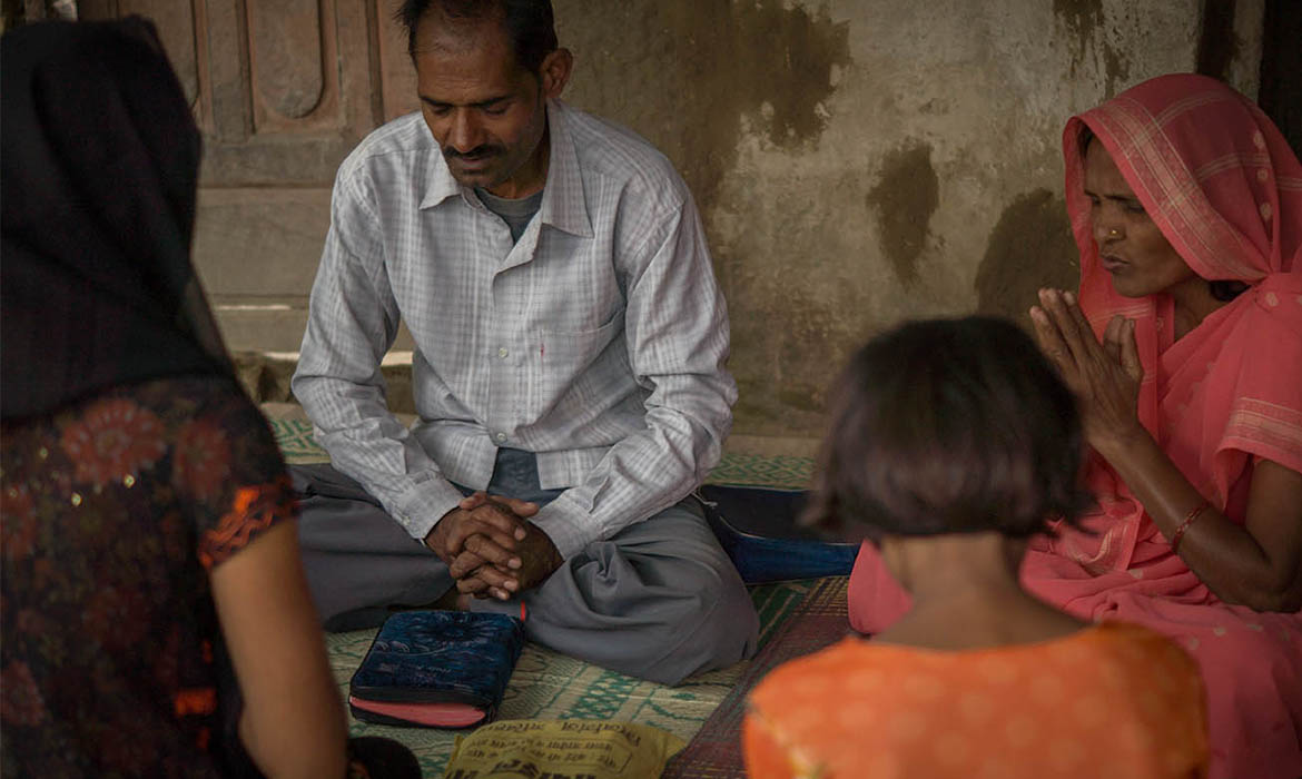 South Asian Christians sitting a carpeted floor praying together