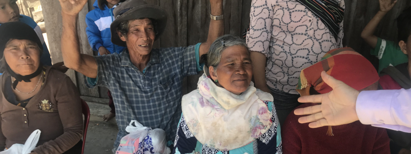Christian missionary extends his hand to elderly Lao woman sitting in a chair