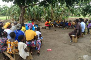 Togolese Christians sitting on rows of wooden benches under a tree for church