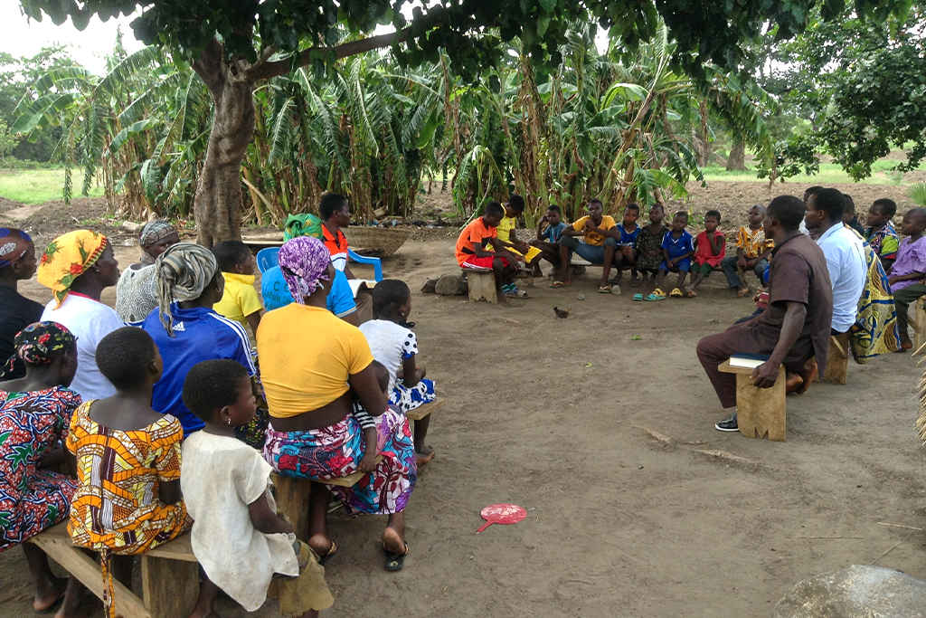 Togolese Christians sitting on rows of wooden benches under a tree for church