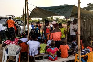Liberian Christian men and women teach children the gospel while they sit under a pavilion made from a tarp and bamboo