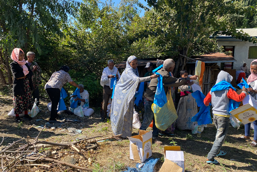 Ethiopian men and women take blue t-shirts from cardboard boxes and grocery bags