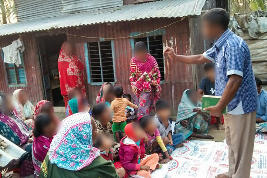 Christian missionary teaches Bangladeshi women and children about Jesus Christ while they sit on the ground