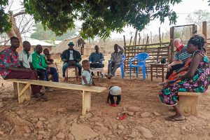 Togolese Christians sitting on plastic chairs and wooden benches under a tree for a bible study