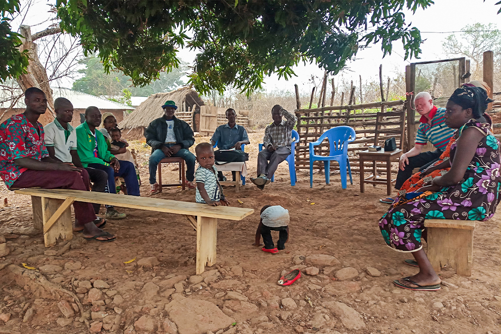 Togolese Christians sitting on plastic chairs and wooden benches under a tree for a bible study