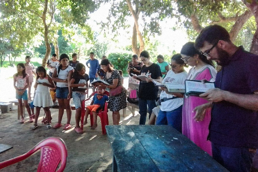 Christians in Colombia stand at tables and benches reading the Bible together
