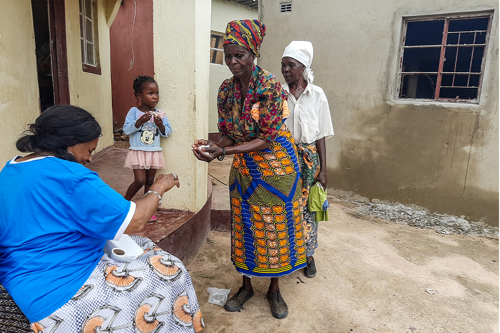 Zimbabwean woman handing cotton balls to another woman outside of her home