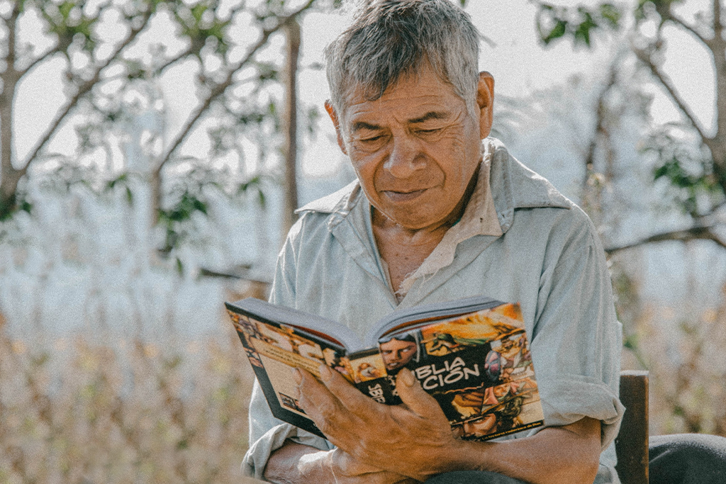 Mexican man sits outside in chair reading a Christian action bible.