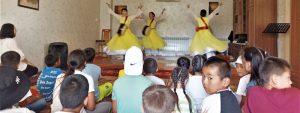 Three Kyrgyz teenage girls perform a traditional dance for school children