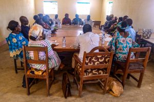 Chadian Christians sit in wooden chairs around a wooden table for a meeting
