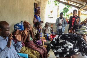 Sierra Leonean Christians sitting in chairs on a porch with their hands up while praying together