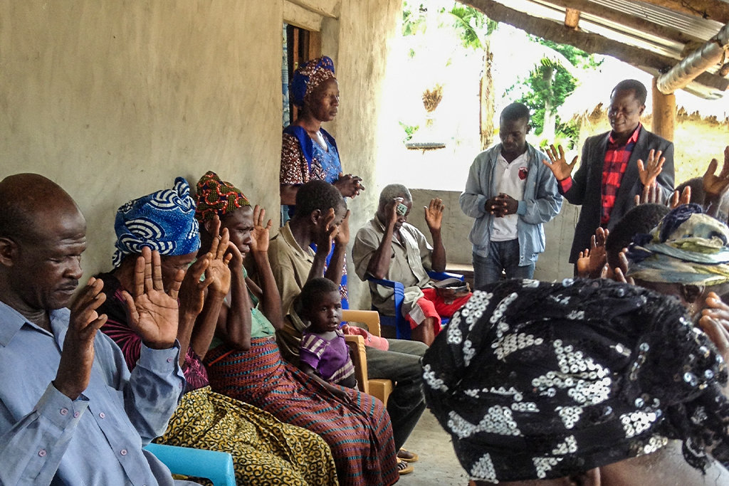 Sierra Leonean Christians sitting in chairs on a porch with their hands up while praying together