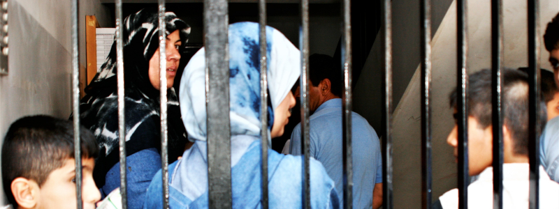 Lebanese women, boys, and man stand behind gate in concrete building
