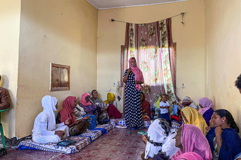 Ethiopian Christian woman standing leading other women sitting on cushions on the floor in singing praises to God