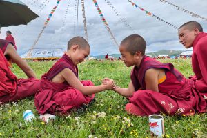 Two Chinese boys wearing traditional Chinese clothing sit in a grassy field arm wrestling