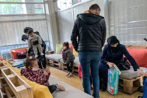 Middle Eastern refugees sit on couches made of wooden pallets while gathering supplies for their children