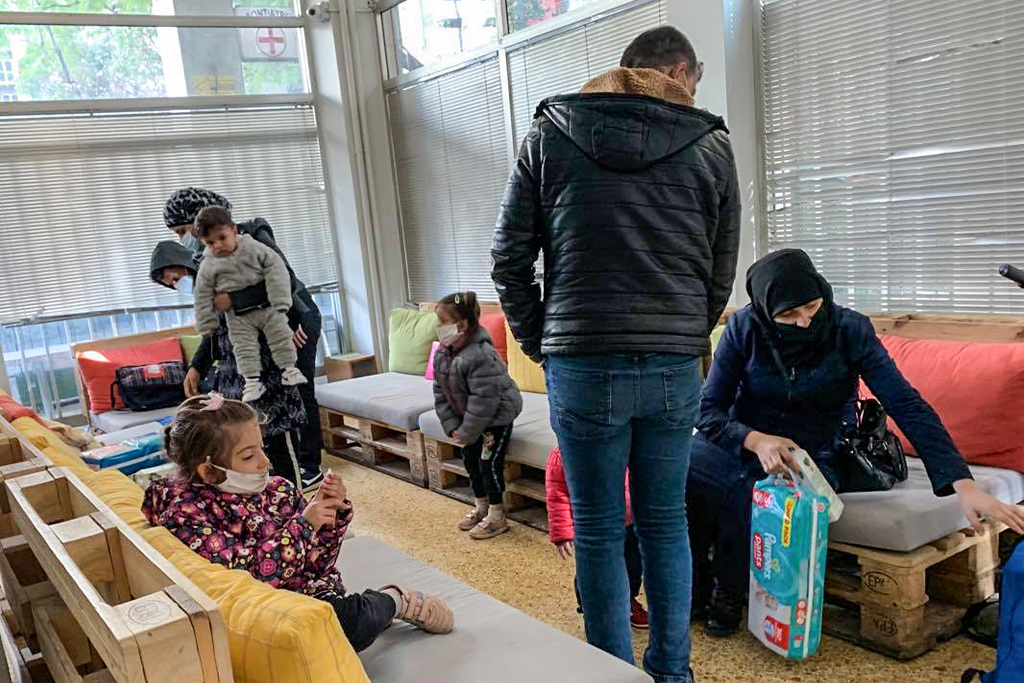 Middle Eastern refugees sit on couches made of wooden pallets while gathering supplies for their children
