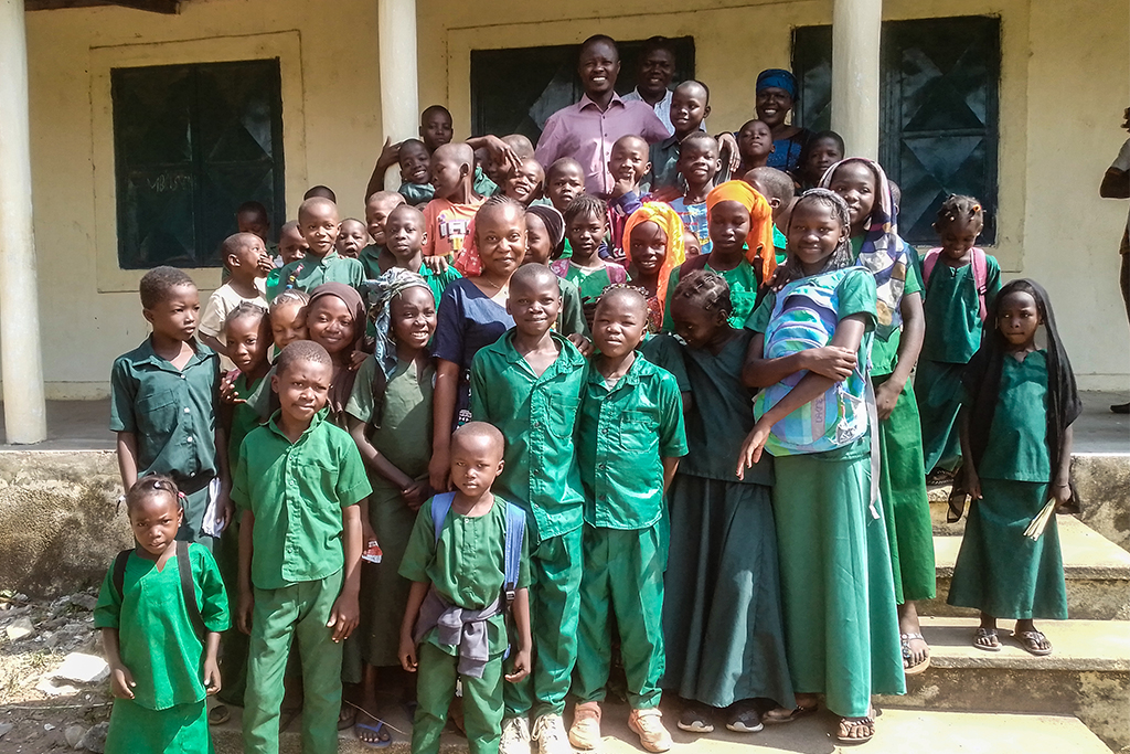 Chadian children stand on the steps of their school wearing their school uniforms of all green.