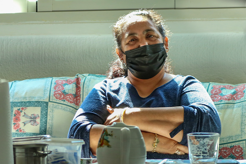 Spanish woman sitting on a couch with her arms folded and a mask on