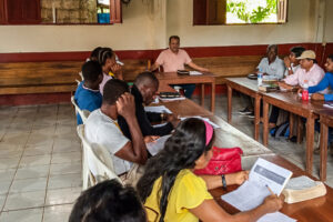 Ecuadorian Christian man leads a Bible study while others sit at wooden tables listening