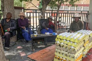 Chinese farmers sitting outside with hats on and cartons of hundreds of eggs sitting on a table