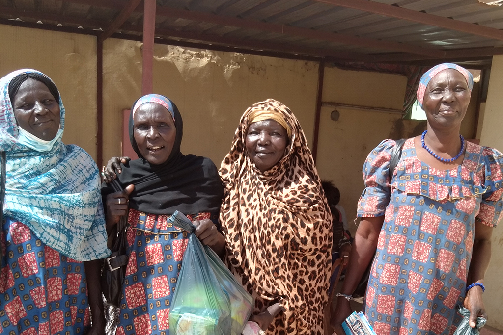 African woman wearing heads coverings and holds groceries in bags