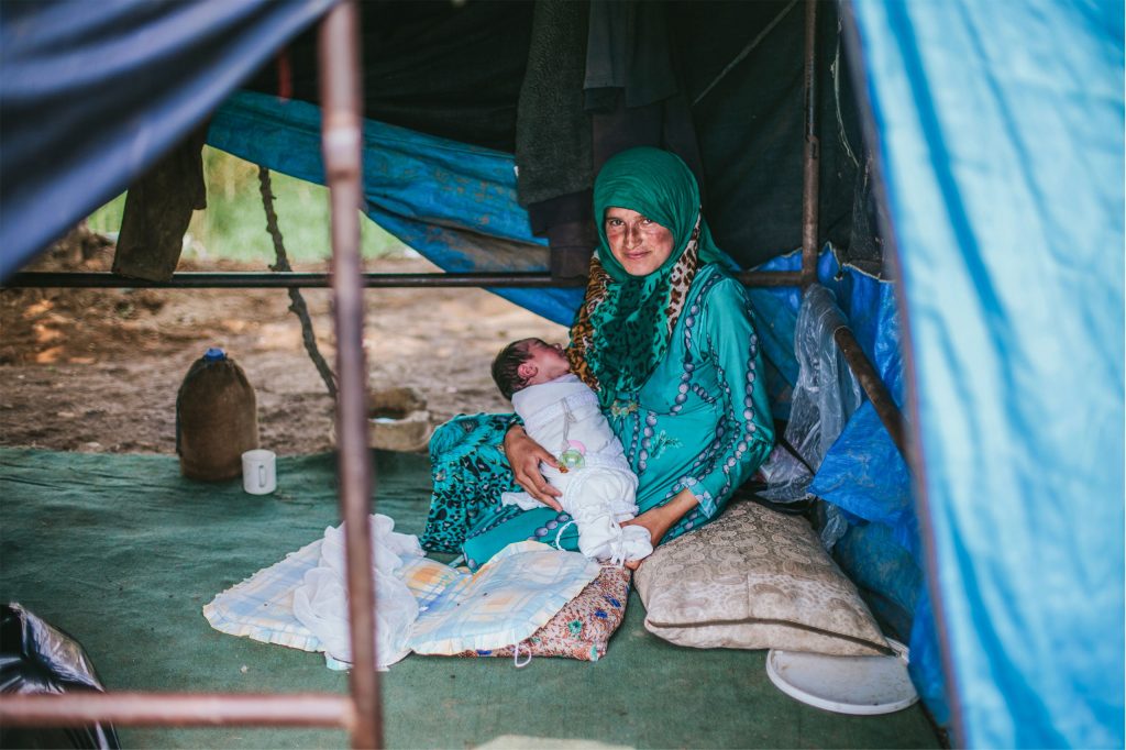 Refugee woman sits in a makeshift tent holding her baby
