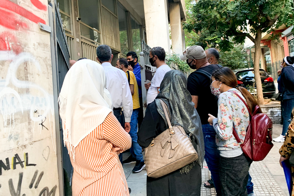 Refugees in Greece wearing masks waiting outside of a government building