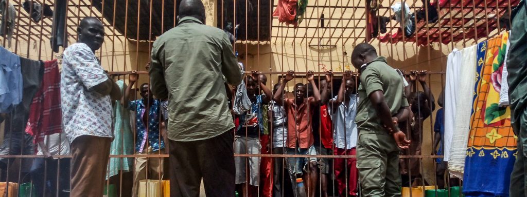 Jail inmates in Mali stand with their hands gripping the metal bars of their cell while a Christian missionary stands on the other side preaching the gospel