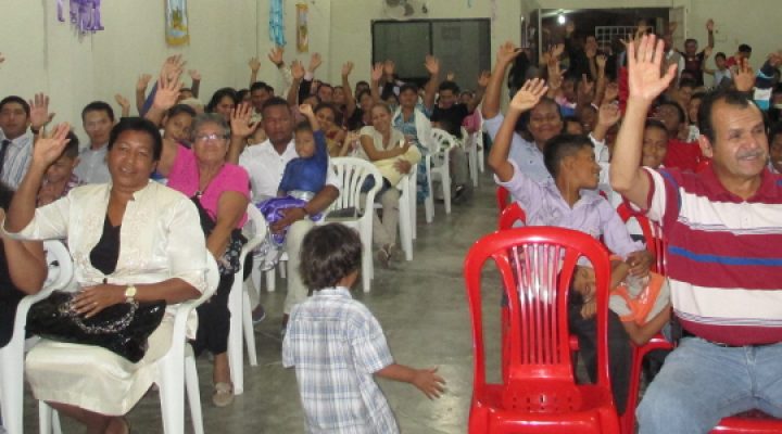 Ecuadorian Christians sitting plastic yard chairs for church and raising their hands