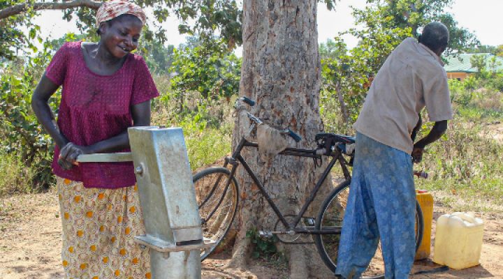 Nigerian woman pumps water from her community water pump while a man grabs something from his bike