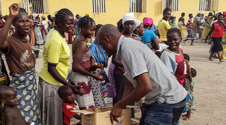 Man pulls essential supplies from a cardboard box to give to a group of Nigerian women and their children