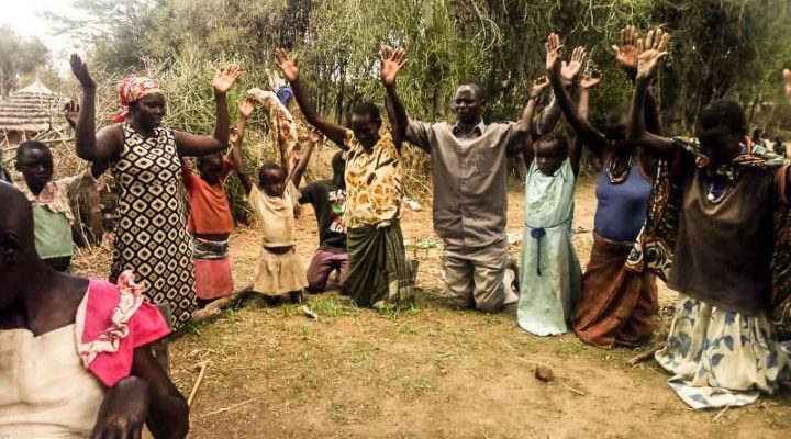 Ugandan Christians on their knees in a circle with their hands lifted praying and praising God