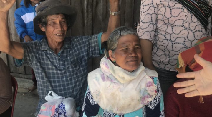 Christian missionary extends his hand to elderly Lao woman sitting in a chair