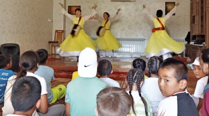 Three Kyrgyz teenage girls perform a traditional dance for school children